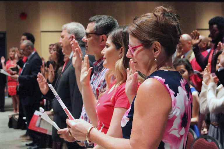 Men and women stand in a row with their rights hands raised as they take the oath of citizenship.