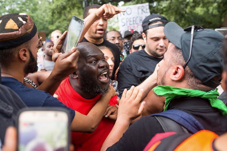 In the middle of a crowd of opposing protesters, two men stand face to face, yelling at each other.