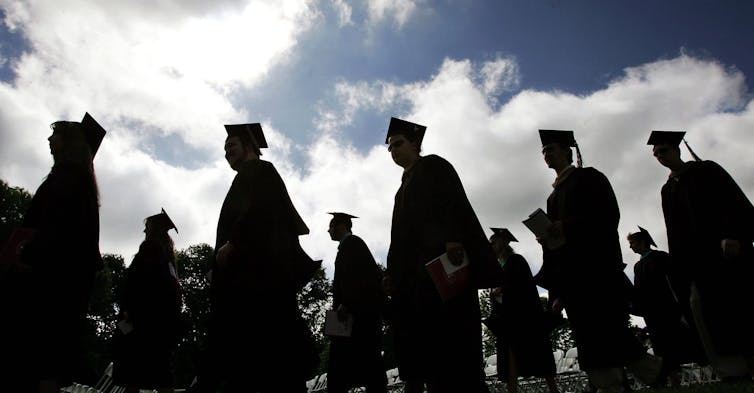Graduates seen in a line in caps and gowns.