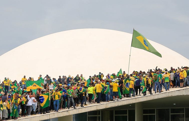 Decenas de manifestantes vestidos de amarillo y verde se paran en una estructura con una cúpula blanca en el fondo.