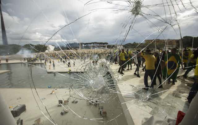 Protesters in yellow and green are seen through a smashed window.