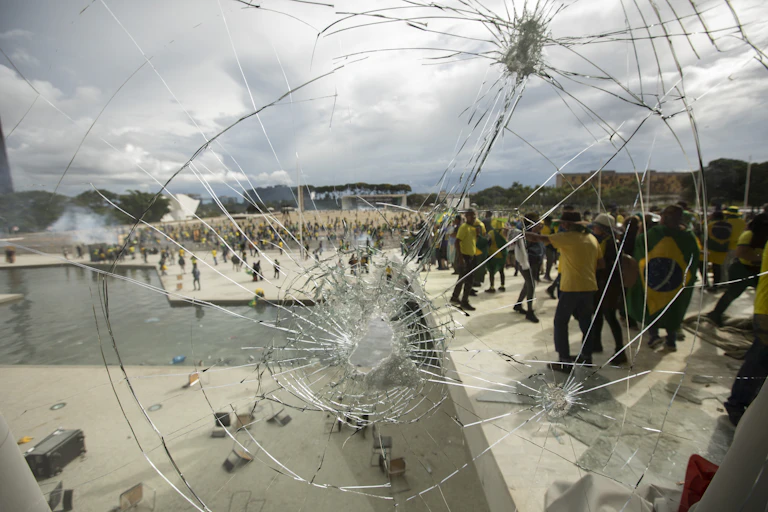 Protesters in yellow and green are seen through a smashed window.