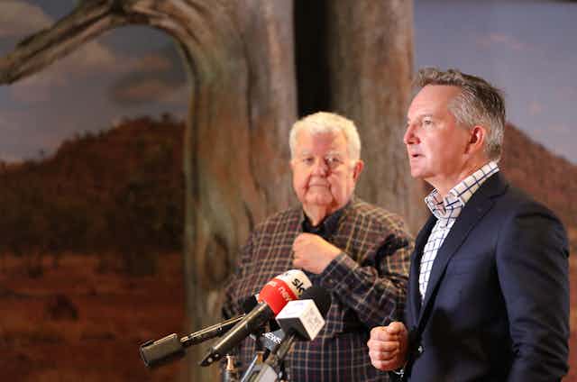 two men stand at microphone