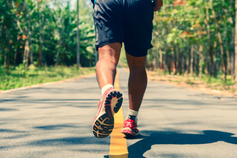 A photo of a man's legs and feet as he runs down an empty road.