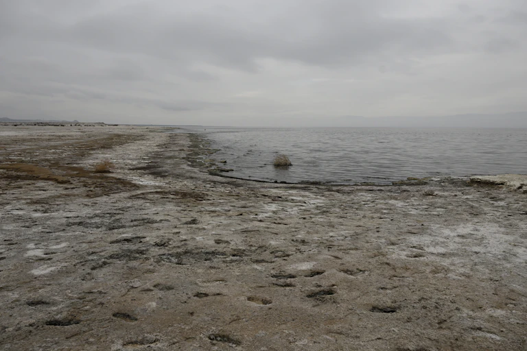 Dusty shoreline with salt crustings along the edge of a large lake.