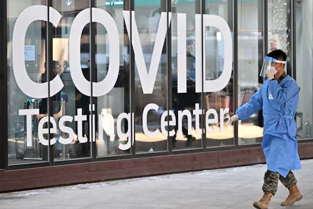 Un homme asiatique en tenue de protection passe devant une devanture de zone de test Covid