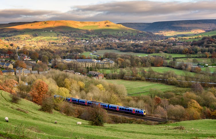 Passenger train passing through british countryside with mountains and town in distance.