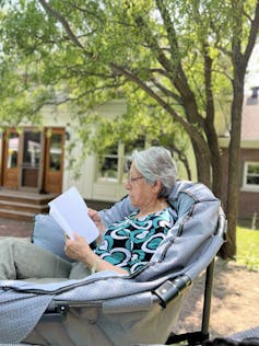 An older woman sitting outside reading a book