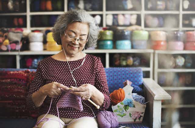 An older woman listening to music on her phone and knitting