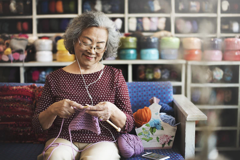 An older woman listening to music on her phone and knitting