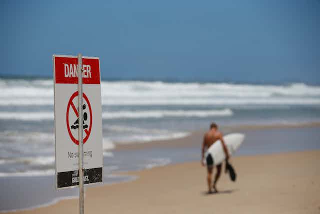 Danger sign at beach with surfer walking