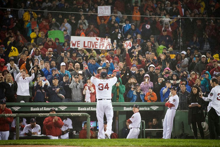 Baseball player raises arms before a cheering crowd.