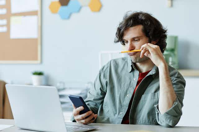 Student looking at his phone with his laptop open