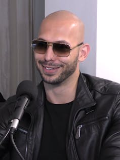 A close-up portrait of a man with a bald head wearing sunglasses and a black leather jacket.