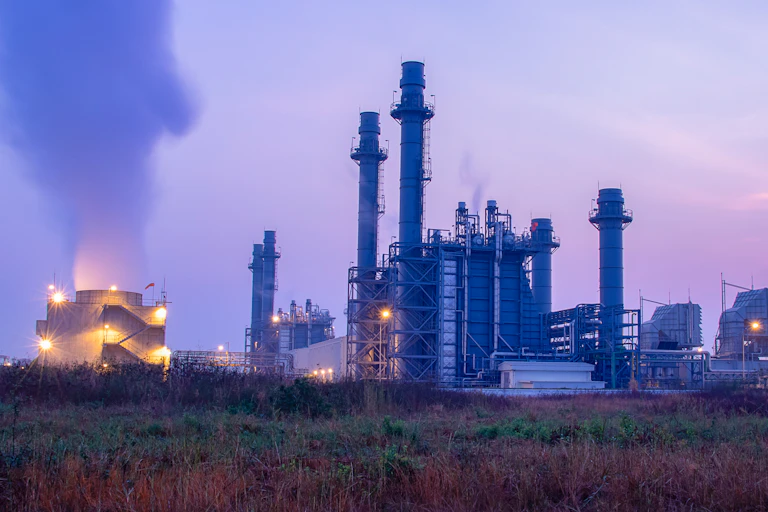 An industrial scene with cooling towers producing steam at dusk.