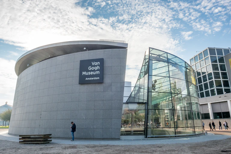 Amsterdam's Van Gogh Museum on a sunny day. The building is round, half constructed from concrete, half glass.