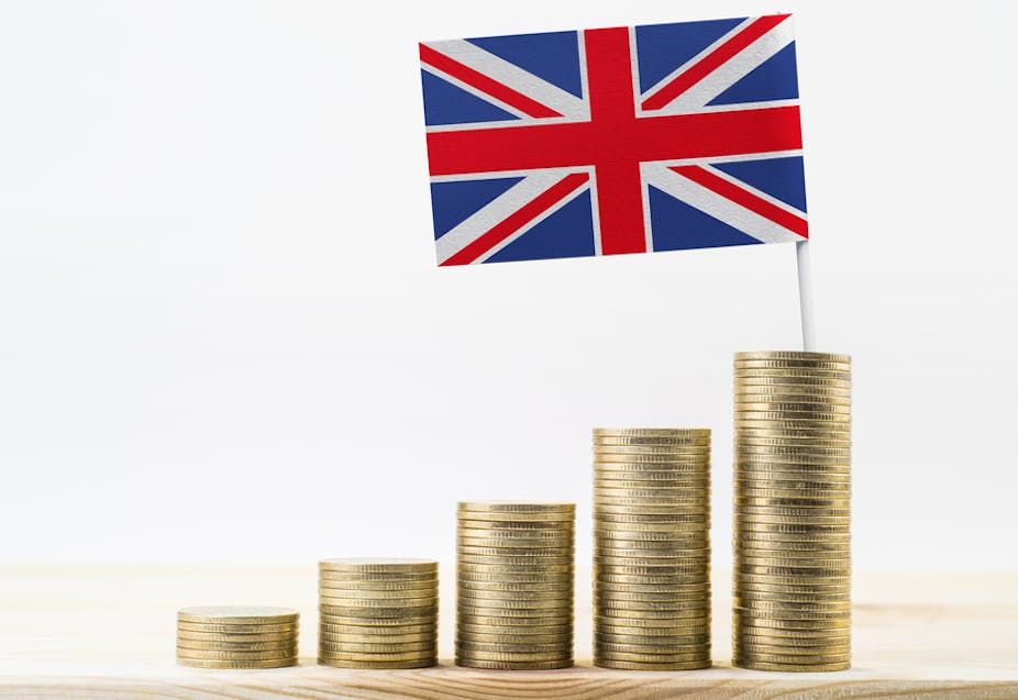 Stacks of gold coins (pound coins) growing with United kingdom flag (UK) on the largest, on a wooden shelf.