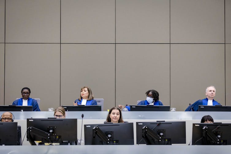 Judges at the ICC, wearing blue robes, sit side by side behind a desk at the ICC