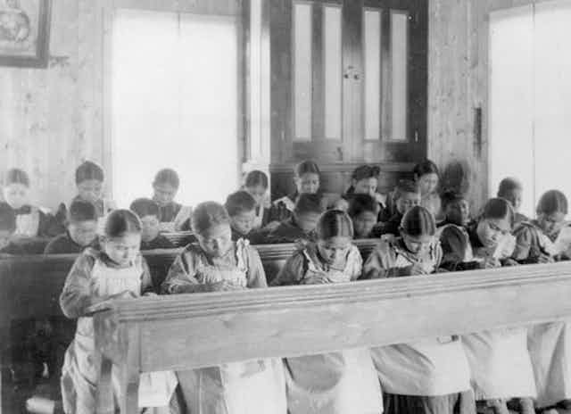 Black and white old photo of children in three rows at school in uniform. 