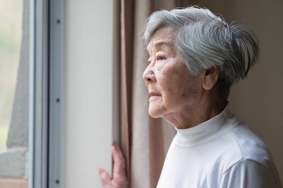 An Asian woman in her 90s looks out the window.