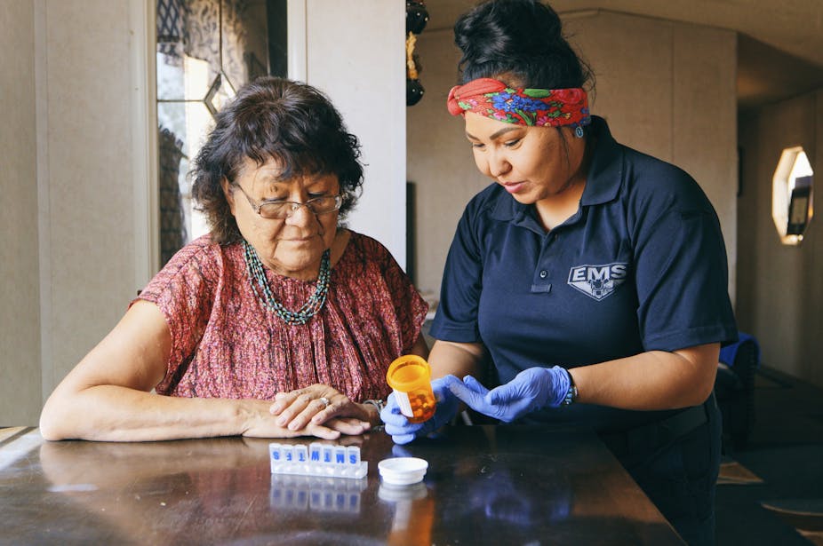 An older Navajo woman receiving health care assistance from someone wearing a shirt emblazoned with the letters E-M-S.