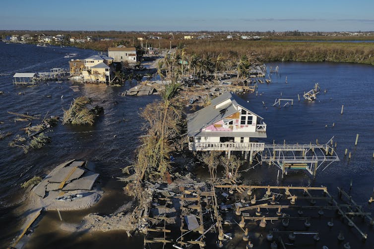 Houses on a road, now underwater, are torn apart, with water on both sides.