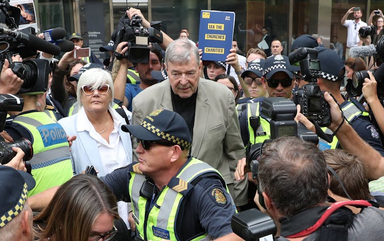 Cardinal George Pell surrounded by police and media leaving a Melbourne court in February 2019.