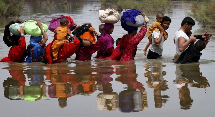 people holding belongings wade through water