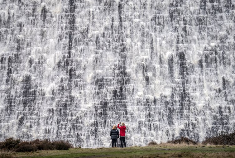 People look on as water pours down the front of a dam