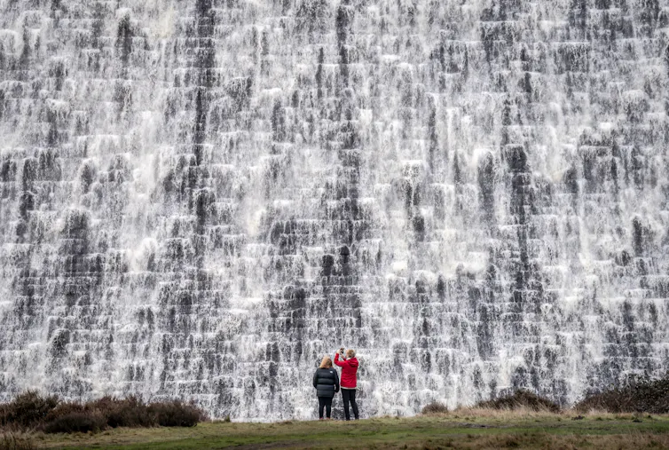 People look on as water pours down the front of a dam