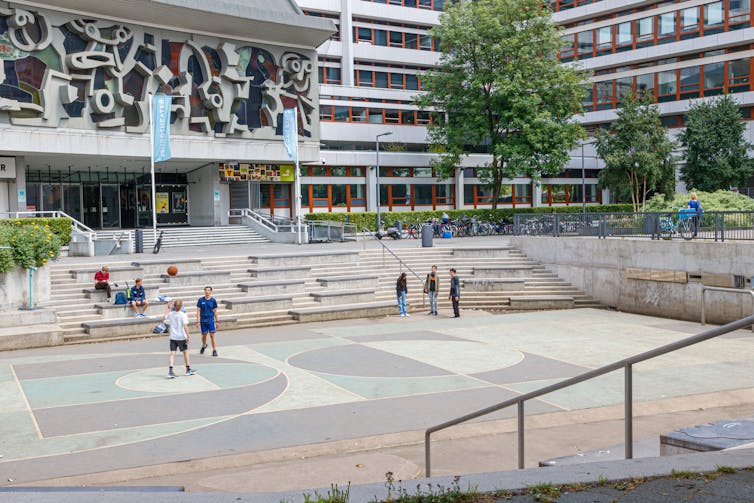 Stairs surround a sunken city plaza being used by people to play with a basketball