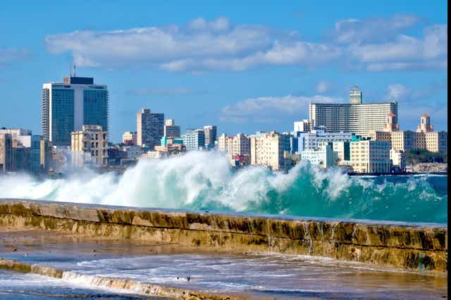 A photo of waves crashing over a seawall, with city buildings in the background.