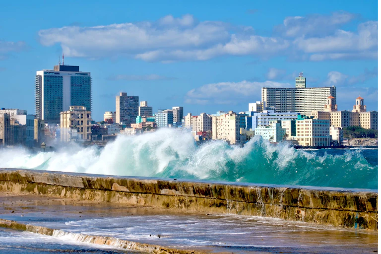 A photo of waves crashing over a seawall, with city buildings in the background.