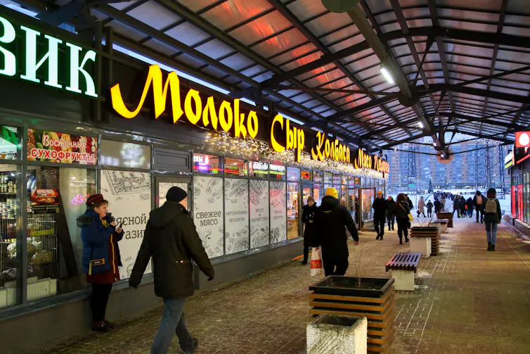 People walking past Russian shops at night.