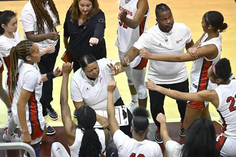 A group of young basketball players gathers around a coach.