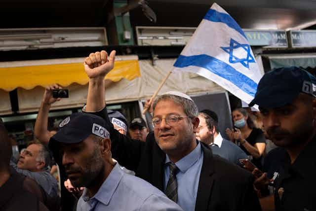 A man raises a fist in a crowd, while behind him someone holds up an Israeli flag.