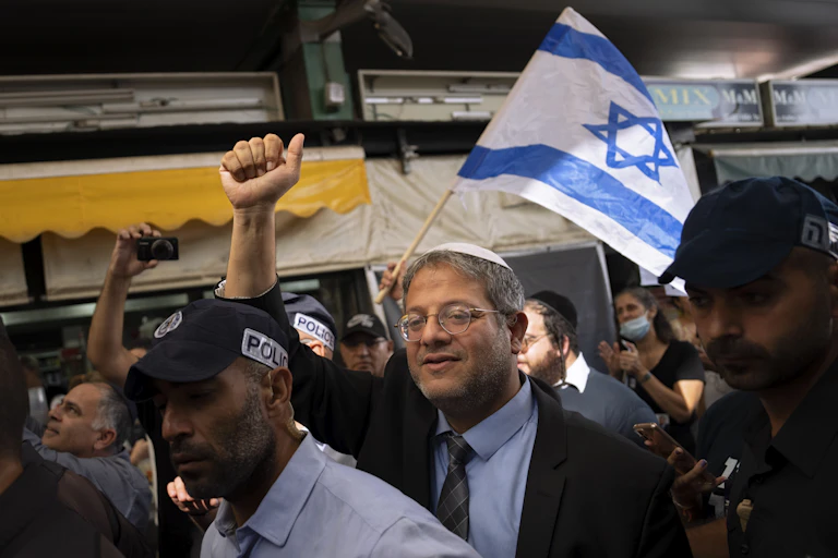 A man raises a fist in a crowd, while behind him someone holds up an Israeli flag.