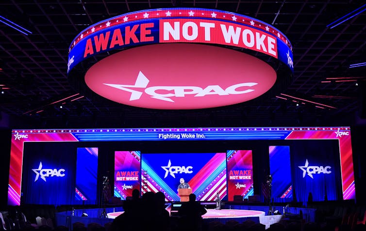 Under the words Awake and Not Woke, workers prepare a stage for a conference with conservative Republicans.