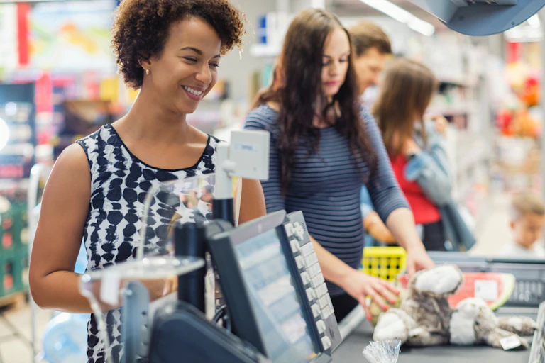 Woman buying goods in a grocery store with a queue in the background.
