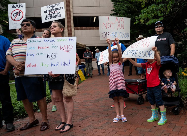 A group of parents and children are holding up posters during a demonstration against teaching race in schools.