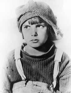 Black and white portrait of a boy wearing a knit hat and overalls.