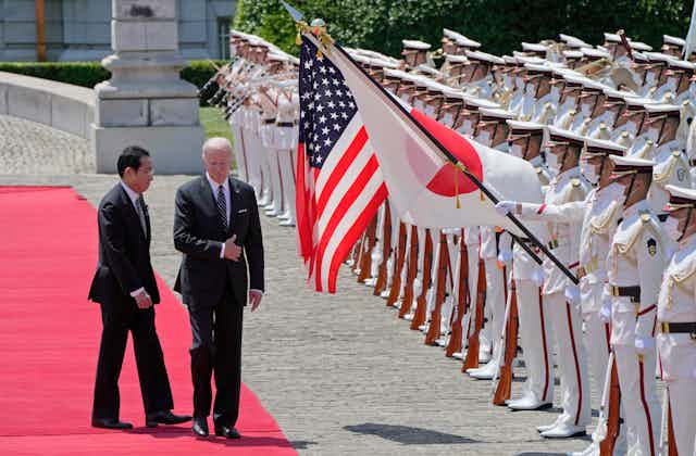Two men in dark suits walk down a red carpet next to guards holding aloft the flags of JaEugene Hoshiko - Pool/Getty Imagespan and the United States.