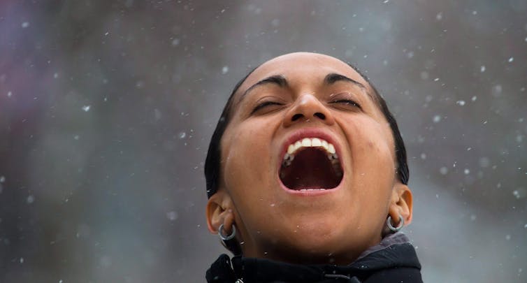 A person catching snow in their mouth smiling.