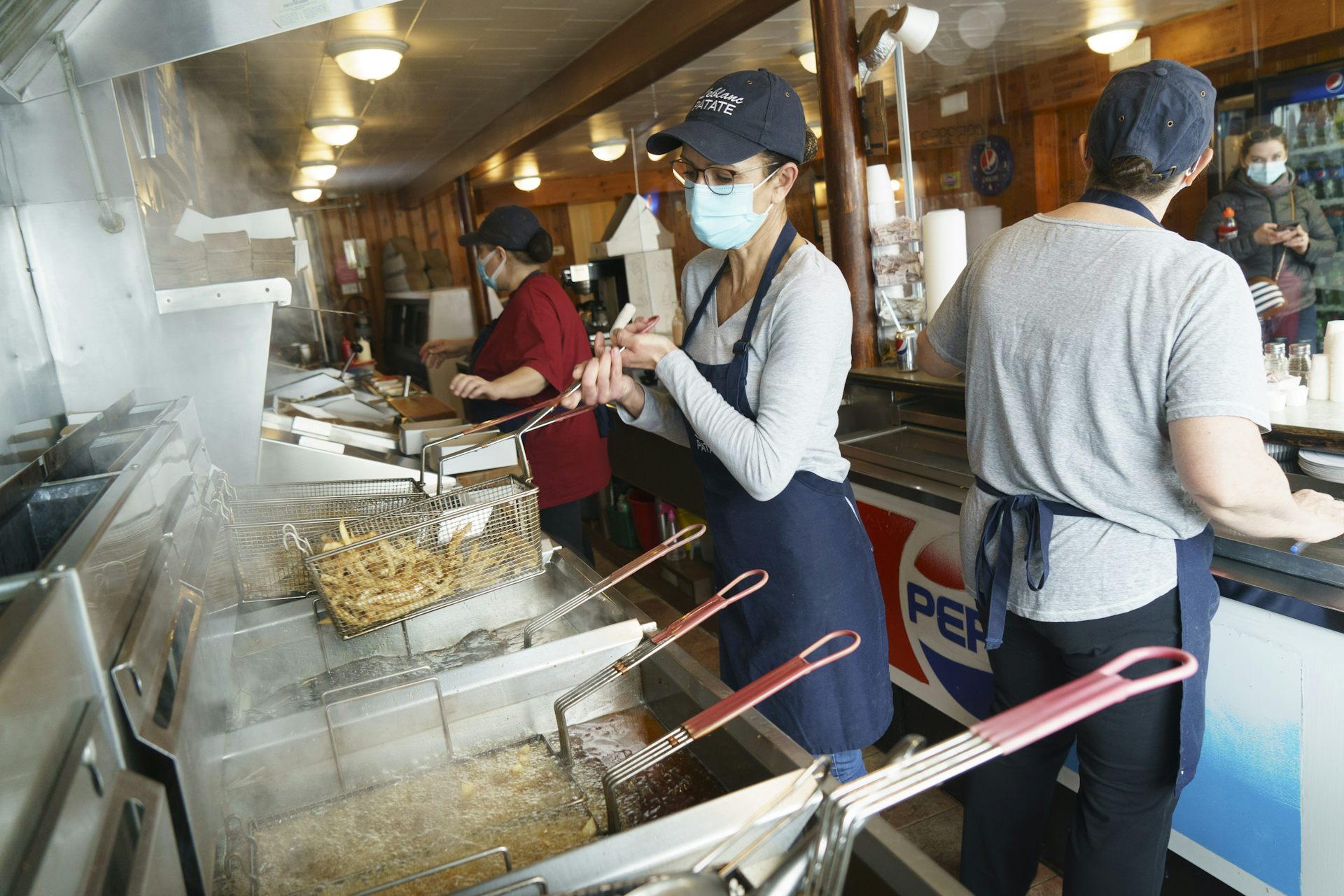 A woman wearing a mask makes French fries in a restaurant kitchen.