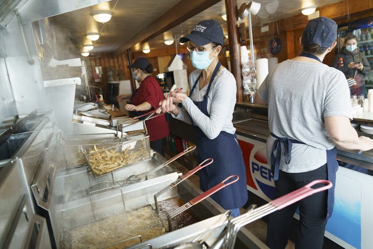 A woman wearing a mask makes French fries in a restaurant kitchen.