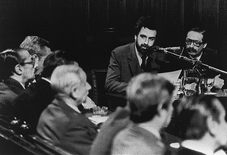 A black and white photo shows two seated male lawyers with facial hair.