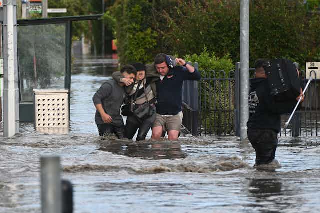 Three men rescue a woman and her belongings in a flooded city street