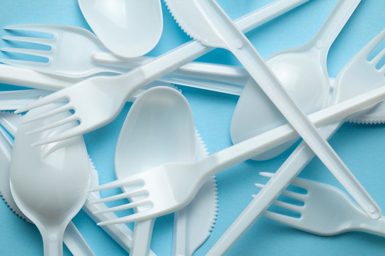 White, plastic forks, knives and spoons on a blue background.