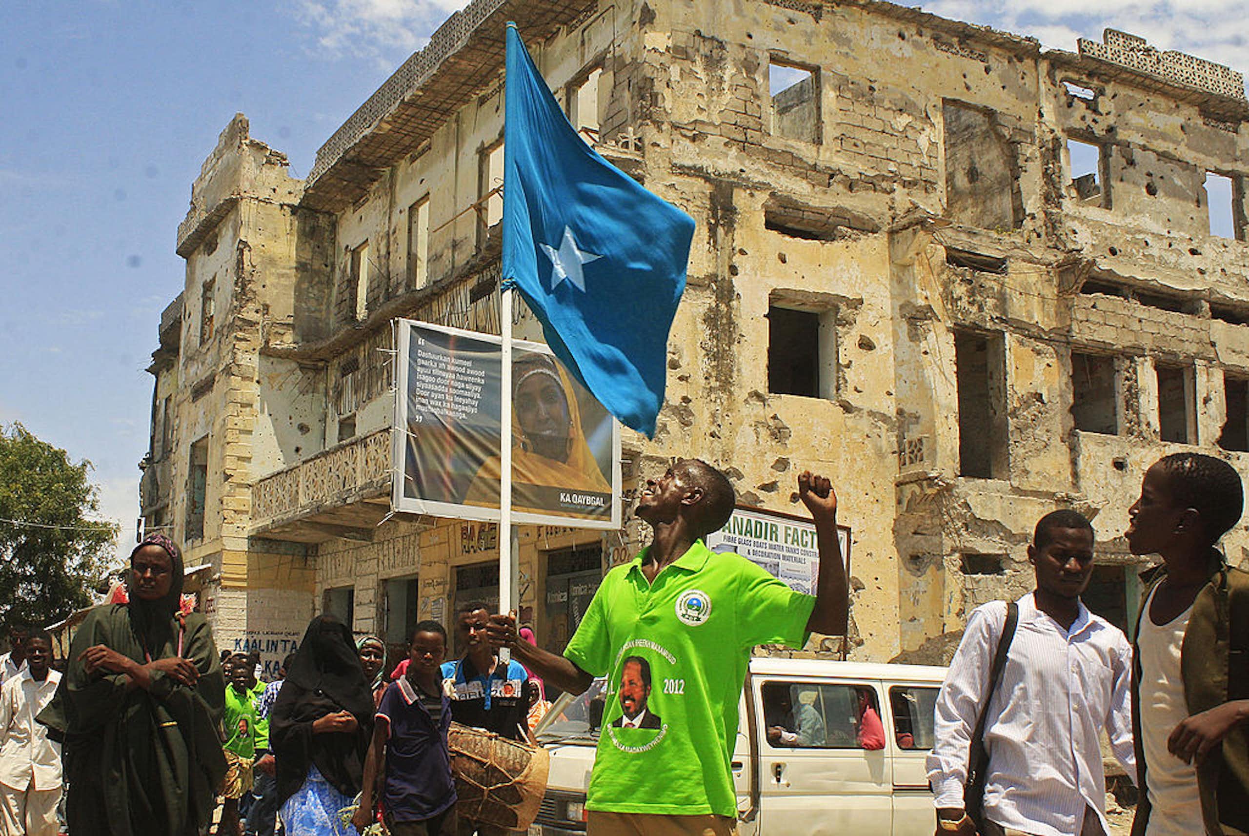 A man waves the Somali flag - blue with a white star in the middle - in front of a bombed-out building.