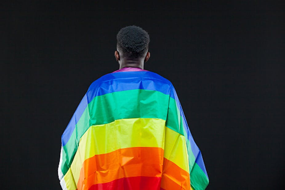 Back view of young African man wrapped in a rainbow flag. 